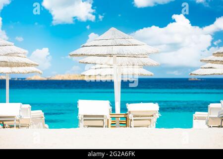 (Fuoco selettivo) splendida vista di alcuni ombrelloni e lettini di paglia bianca su una spiaggia di sabbia bianca bagnata da un bel mare turchese. Foto Stock