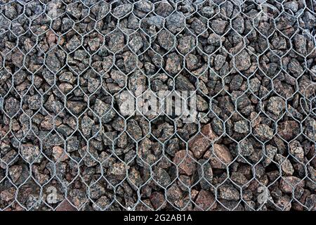 Vista parziale della recinzione gabion riempita con pietre di granito supportate da recinzione catena, sfondo Foto Stock