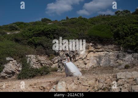 Urla, Izmir, Turchia. 9 Giugno 2021. Sposa appena sposata che cammina con i suoi tacchi nuziali e alti in un percorso in alta temperatura del tempo estivo. Sta tornando in auto da una sessione fotografica in una baia nella città turistica di Urla di Izmir. Credit: Uygar Ozel/ZUMA Wire/Alamy Live News Foto Stock