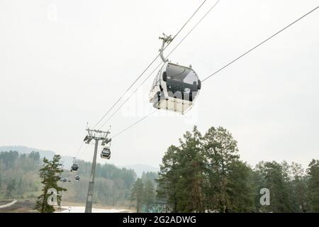 Cabine di ascensore in una stazione sciistica di montagna. Pista di risalita sulla stazione invernale di montagna hilghland in giornata nuvolosa. Funivia per la seggiovia con le persone. Scenico Foto Stock