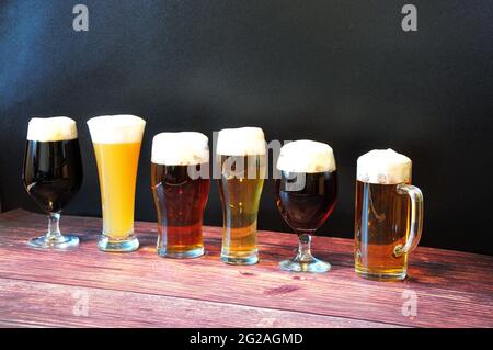 Sei bicchieri diversi con diversi tipi di birra sono in fila su un tavolo di legno. Vista laterale. Foto Stock