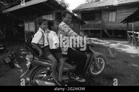 Sungai Uluk Palin, Kapuas Hulu, Kalimantan occidentale, Indonesia. Marzo 2007. I bambini che indossano l'uniforme scolastica lasciano la loro casa situata vicino alla solitudine tradizionale della comunità di Dayak Tamambaloh. Alcuni dei membri del clan Tamambaloh hanno costruito le loro nuove case sul terreno, a parte la longhouse.--fotografato su film bianco e nero, scansionato, digitalizzato. Foto Stock