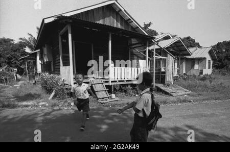 Sungai Uluk Palin, Kapuas Hulu, Kalimantan occidentale, Indonesia. Marzo 2007. I bambini che indossano l'uniforme scolastica lasciano la loro casa situata vicino alla solitudine tradizionale della comunità di Dayak Tamambaloh. Alcuni dei membri del clan Tamambaloh hanno costruito le loro nuove case sul terreno, a parte la longhouse.--fotografato su film bianco e nero, scansionato, digitalizzato. Foto Stock