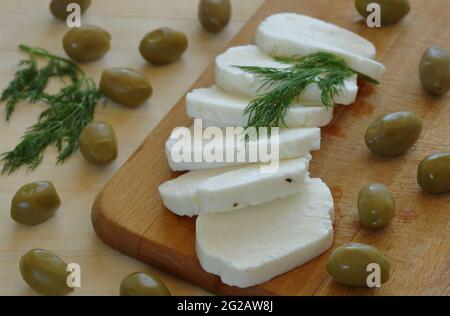 Halloumi di formaggio tradizionale cipriota fresco fatto in casa tagliato in fette decorate con erbe verdi su tavola di legno e primo piano tavolo. Foto Stock