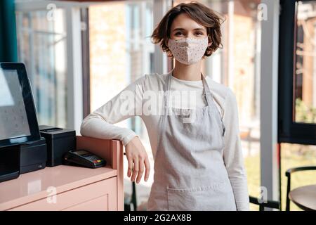 Felice proprietario di caffè femminile indossando maschera protettiva viso, riapertura dopo l'epidemia di coronavirus Foto Stock