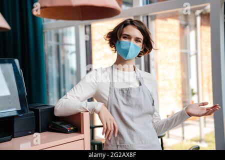 Felice proprietario di caffè femminile indossando maschera protettiva viso, riapertura dopo l'epidemia di coronavirus Foto Stock