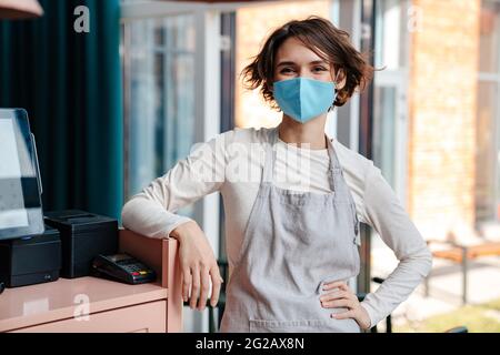 Felice proprietario di caffè femminile indossando maschera protettiva viso, riapertura dopo l'epidemia di coronavirus Foto Stock