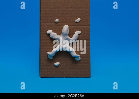 Un manichino bianco di plastilina che pratica l'arrampicata sportiva su sfondo blu. La bambola sta arrampicando su una parete di cartoncino con le maniglie di plastilina. Foto Stock