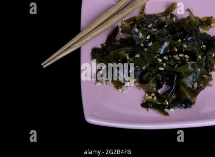 Alghe wakame idratate con semi di sesamo su un piatto accanto ai trichetti su sfondo nero Foto Stock