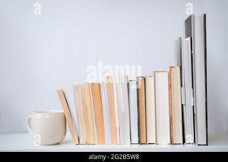 tazza da tè per caffè accanto a una pila di libri. Tavola bianca e sfondo. Vista frontale Foto Stock