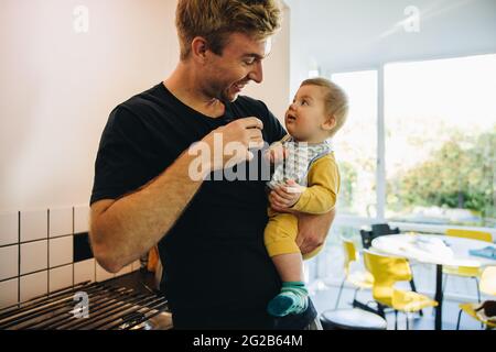 Uomo che porta il figlio e che ha una tazza di caffè. Padre bere caffè tenendo il suo bambino. Foto Stock