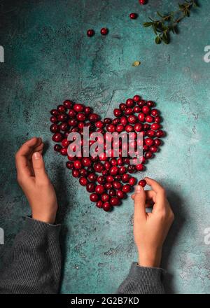 Le mani del bambino fanno una forma del cuore con i mirtilli del mirtillo rosso bacche. Concetto di cibo vegano sano. Foto Stock