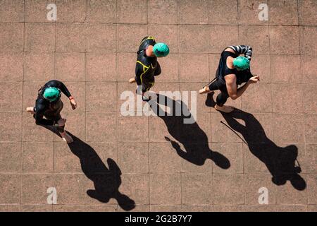 I triatleti del London Triathlon 2018 gettano lunghe ombre mentre camminano verso l'inizio della corsa di nuoto, Londra, Regno Unito Foto Stock