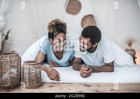 Uomo e donna sorridenti dalla pelle scura che giace sotto la coperta Foto Stock