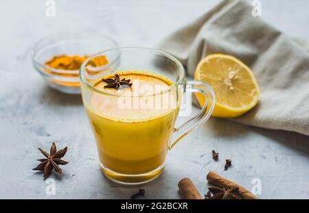 Un bel bicchiere con latte dorato, curcuma, spezie e limone su sfondo grigio. Sana bevanda ayurvedica. Rafforzare il sistema immunitario. Antioxi Foto Stock