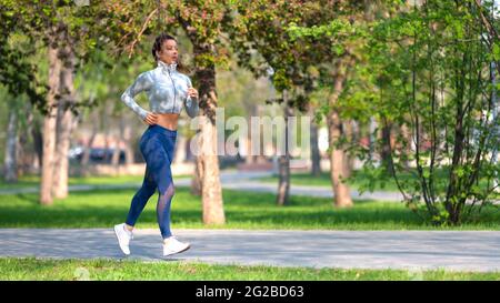 Foto a lunghezza intera di una donna che corre nel parco nelle prime ore del mattino. Donna attraente che si adatta e sano. Concetto di stile di vita sano. Formato 16x Foto Stock