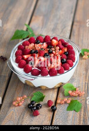 Lampone fatto in casa, fragole, ribes nero e rosa dessert, cheesecake, trifle, topo in un bicchiere su un tavolo di legno in giardino. Foto Stock