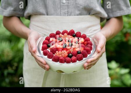 Delizioso lampone, fragole, dessert di ribes nero e rosa, cheesecake, trifle, mouse in mani femminili in giardino. Foto Stock