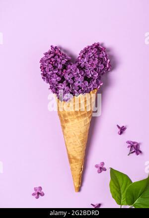 Astratto vita morta di un cono di cialda gelato con fiori commestibili lilla a forma di cuore su sfondo rosa. Foto Stock