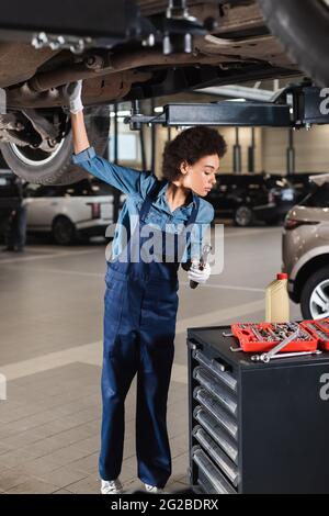 giovane meccanico afroamericano che lavora sotto l'auto in garage Foto Stock