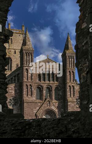 I bordi macabri di una finestra vuota nel palazzo vescovile del 14th ° secolo, accanto alla cattedrale di St Davids a Pembrokeshire, Galles, Regno Unito, incorniciano la torre centrale della cattedrale e il suo fronte ovest, Ricostruito in arenaria viola in stili misti e con standard tecnici insoddisfacenti nel 1793 dal celebre architetto neoclassico Regency e Georgiano John Nash, designer di Buckingham Palace, Marble Arch e Regent Street di Londra, e dal Royal Pavilion di Brighton. La facciata doveva essere rimodellata negli anni '1860s, quando iniziò a piegarsi verso l'esterno e necessitò di ulteriori riparazioni importanti negli anni '1990s. Foto Stock