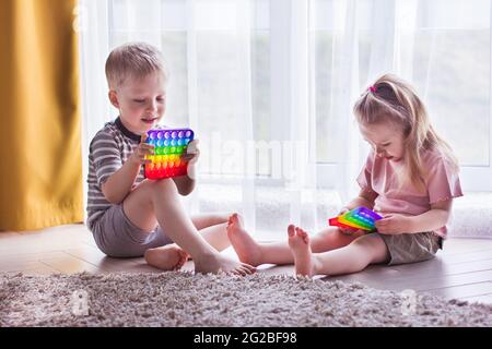 Biondo ragazzo e ragazza i bambini giocano con il giocattolo sensoriale pop it. Gioco trendy in silicio per bambini e adulti stressati. Giocattoli morbidi squishy della bolla. Bambini p Foto Stock