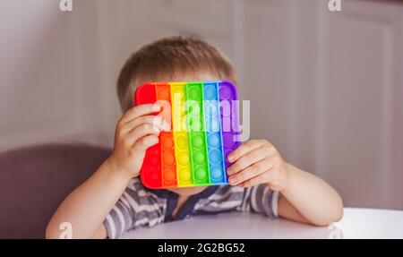 Ragazzo biondo che gioca con iridow pop it fidget giocattolo. Giocattolo sensoriale Fidget a bolla - giocattolo lavabile e riutilizzabile per alleviare lo stress. Giocattolo antistress per bambini Foto Stock