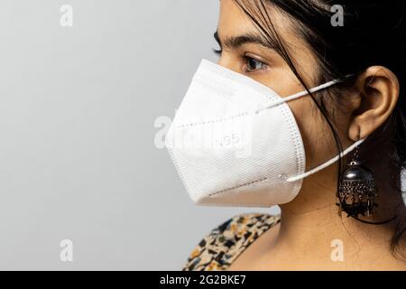 Primo piano faccia laterale di una donna indiana che indossa una maschera N 95 su sfondo bianco Foto Stock