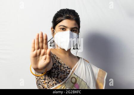 Una donna indiana in saree che indossa una maschera naso N 95 che mostra palma come divaricarsi sociale su sfondo bianco Foto Stock