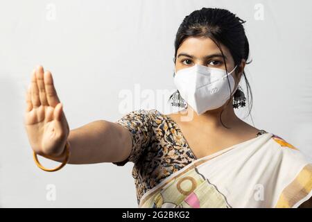 Una donna indiana in saree che indossa una maschera naso N 95 che mostra palma come divaricarsi sociale su sfondo bianco Foto Stock