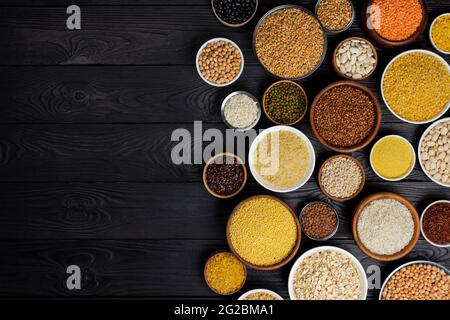 Vari Cereali, granaglie, semi, semole, legumi e fagioli in ciotole in legno nero con sfondo spazio copia Foto Stock