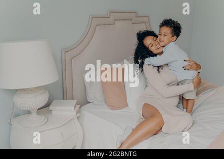 Carino piccolo figlio abbracciando la sua mamma incinta, in attesa di futuro fratello o sorella Foto Stock