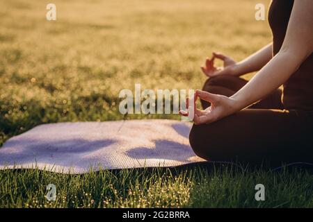 la donna pratica yoga in posizione di loto in una mattina presto soleggiata in erba con rugiada. Concetto di stile di vita sano. Meditazione mattutina, relax. SOF Foto Stock