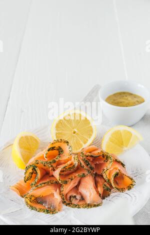 Panini di salmone affumicato con limone su piatto bianco e salsa di senape in ciotola bianca su sfondo di legno bianco, foto di stock vertciale con spazio per la copia Foto Stock