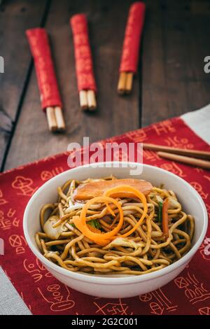 Tagliatelle vegetariane cinesi in una ciotola bianca su tappetino cinese posto su tavolo di legno, foto verticale stock Foto Stock