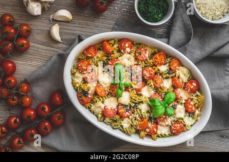 Casseruola di pasta con salsa al pesto al basilico, pomodori e mozzarella, vegetariana, su un vecchio tavolo di legno Foto Stock