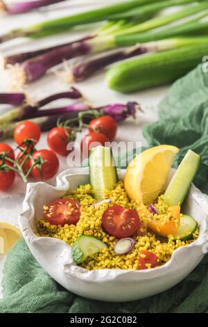 Insalata couscous con cetriolo, pomodori e cipolle in una ciotola bianca, verdure colorate, verticale Foto Stock