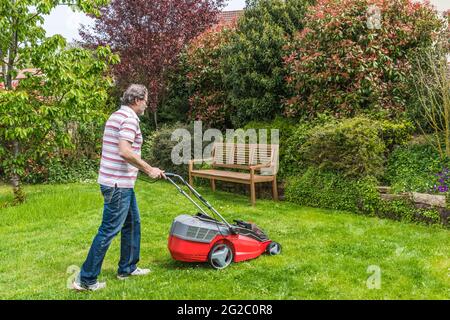 Uomo che taglia il prato nel suo giardino Foto Stock