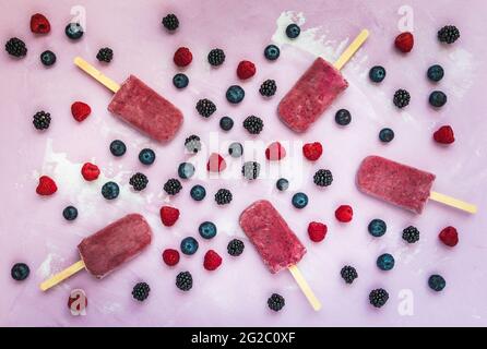 Yogurt alla mirtillo misto fatto in casa, ghiaccioli con frutti di bosco freschi su sfondo rosa, vista dall'alto Foto Stock