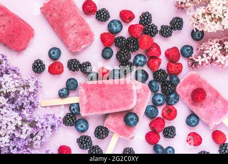 Yogurt alla mirtillo misto fatto in casa, ghiaccioli con frutti di bosco freschi su sfondo rosa, vista dall'alto Foto Stock