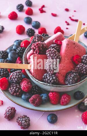 In una ciotola su sfondo rosa, verticale, viene fatto in casa uno yogurt a base di frutti di bosco misti Foto Stock