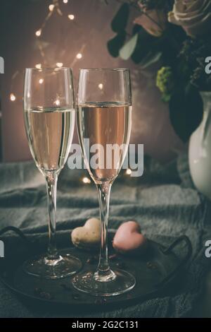 Due bicchieri con vino frizzante e macaron a forma di cuore, luce soffusa, atmosfera romantica, verticale Foto Stock