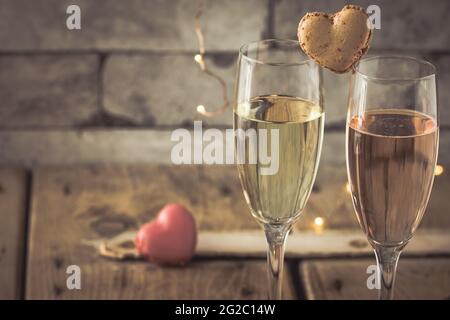 Due bicchieri con vino frizzante e macaron a forma di cuore su un rustico tavolo in legno, atmosfera romantica Foto Stock