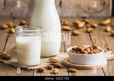 Bicchiere e caraffa con latte di mandorle vegane, noccioli di mandorle e mandorle intere su un vecchio tavolo rustico in legno Foto Stock