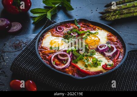 Shakshuka in una padella di ferro. Piatto tradizionale mediorientale. Uova fritte con pomodori, peperone, verdure ed erbe, uova soleggiate con il lato alto. Foto Stock