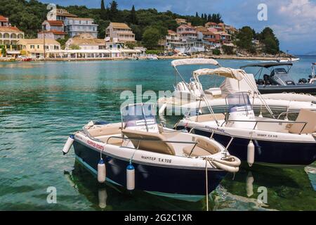 Isola di Corfù/Grecia - 6 maggio 2019: Vista sul bellissimo villaggio di Kassiopi - laguna di mare con acque turchesi calme, barche a motore, case e caffè di strada su ba Foto Stock