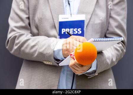 Giornalista femminile a conferenza stampa o evento mediatico, scrivendo note, tenendo il microfono. Concetto di giornalismo broadcast. Foto Stock