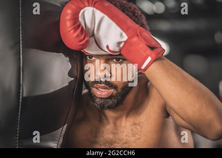 Giovane kickboxer dalla pelle scura che si allena in palestra e che guarda stanco Foto Stock