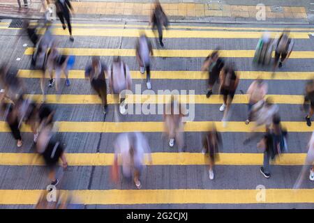 Affollamento di gente assetata o pendolari Crossing Street a Hong Kong, con linee gialle Crosswalk. Attraversamento pedonale giallo zebra Foto Stock