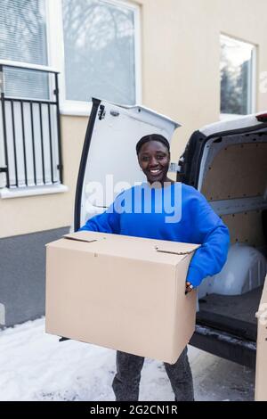 Donna sorridente che porta una scatola di cartone Foto Stock